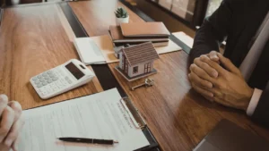 Signature d’un compromis de vente immobilier : documents contractuels, maquette de maison, clés et calculatrice sur une table, illustrant l’avant-contrat lors d’une transaction immobilière.