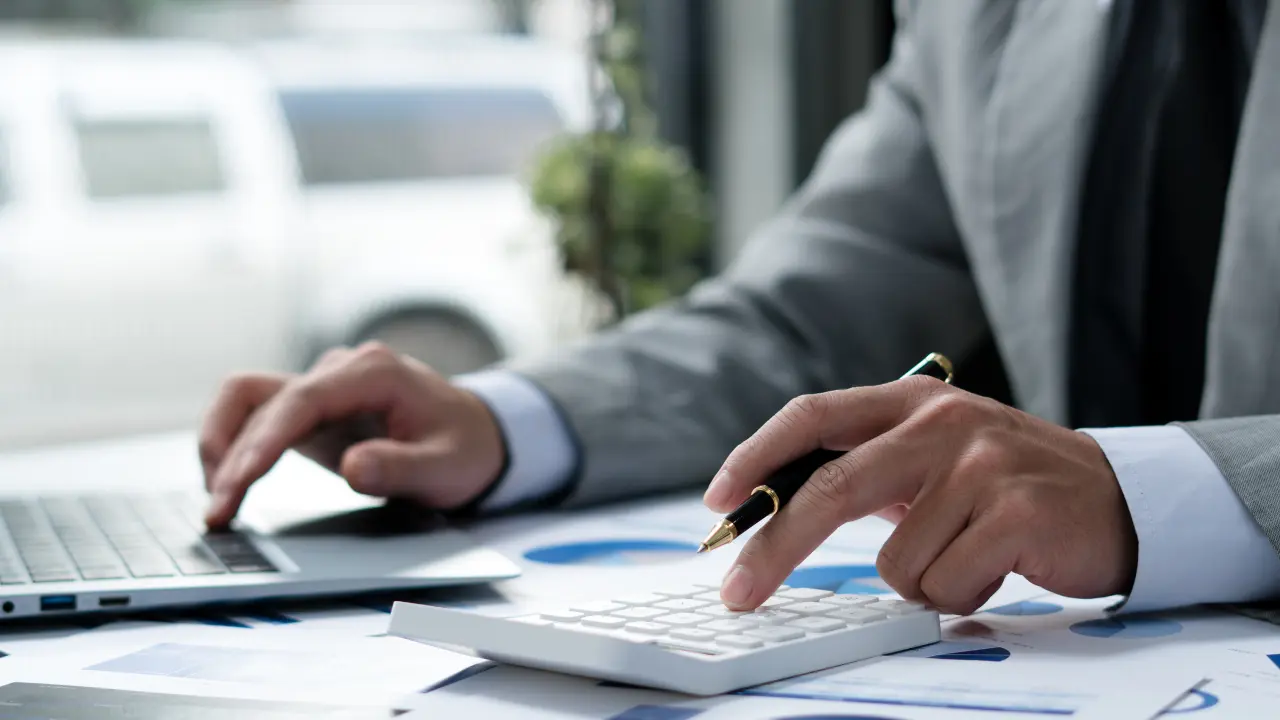 Calcul des frais de notaire lors d’un achat immobilier : personne utilisant une calculatrice et un ordinateur pour estimer les coûts liés à une transaction immobilière.