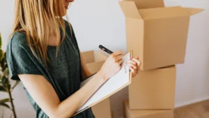 Réalisation d’un état des lieux de sortie : locataire notant l’état du logement devant des cartons de déménagement, illustrant les vérifications lors de la fin de bail.